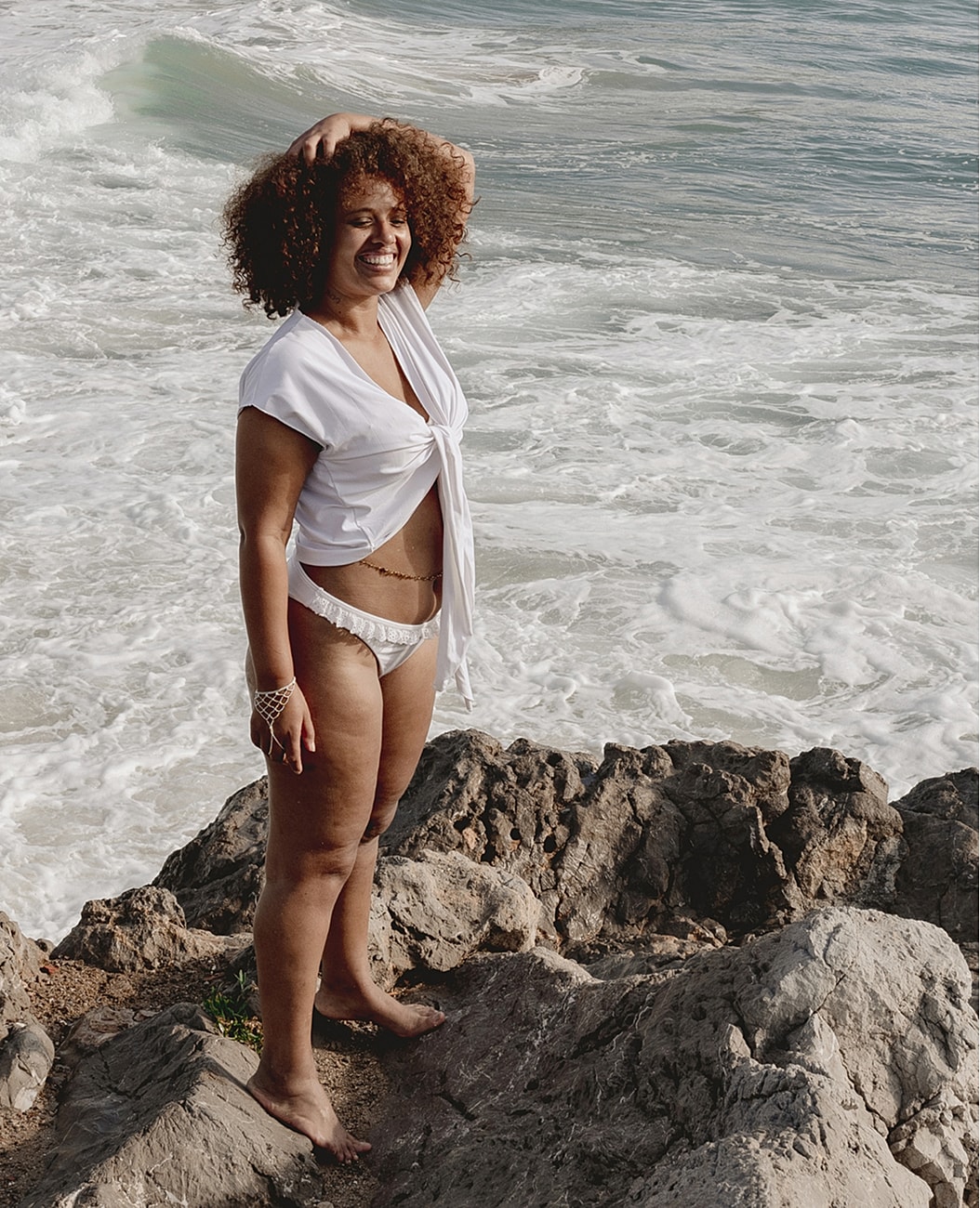 Woman in white outfit standing by ocean waves.