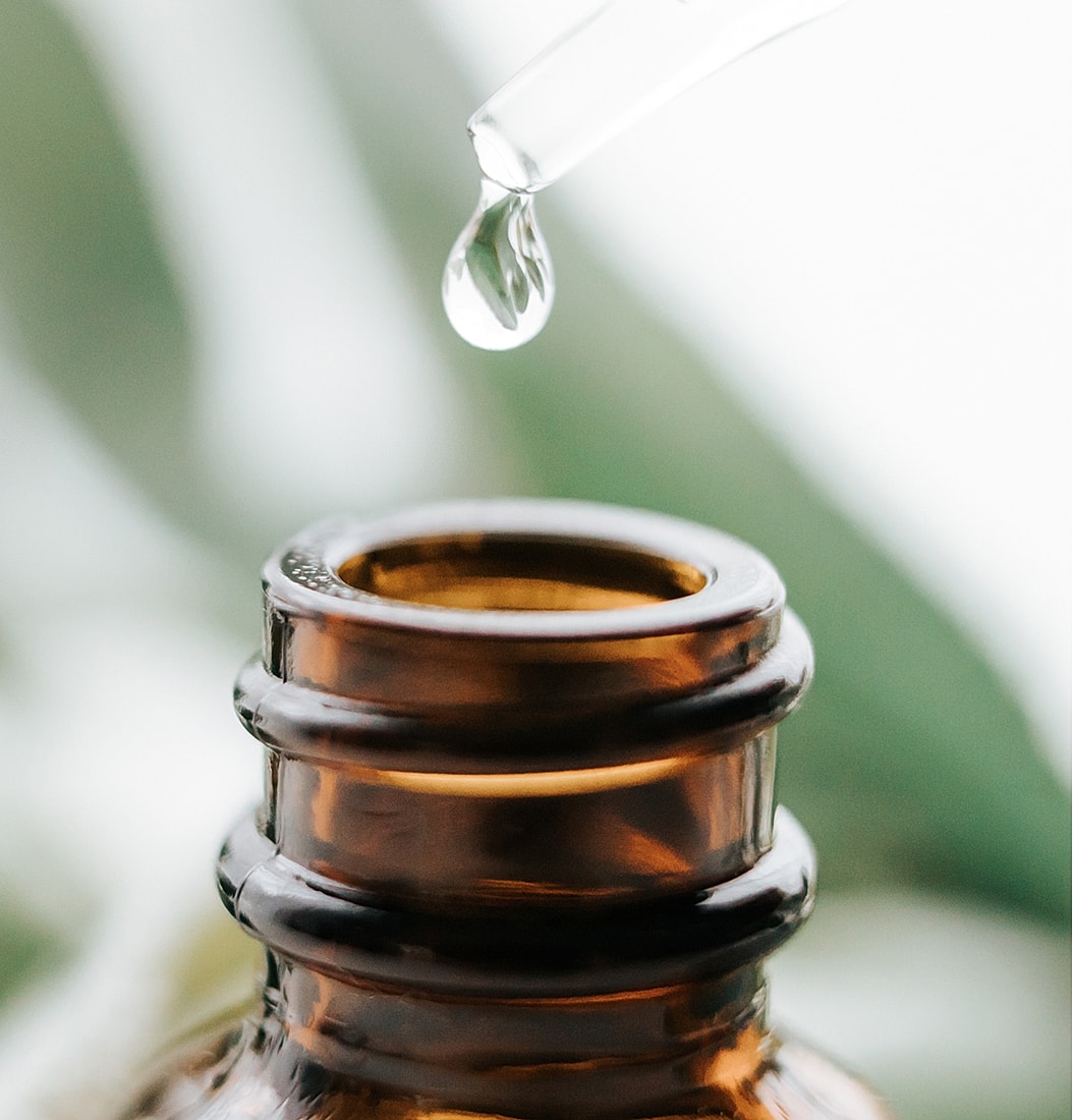 Dropper with oil above brown glass bottle.