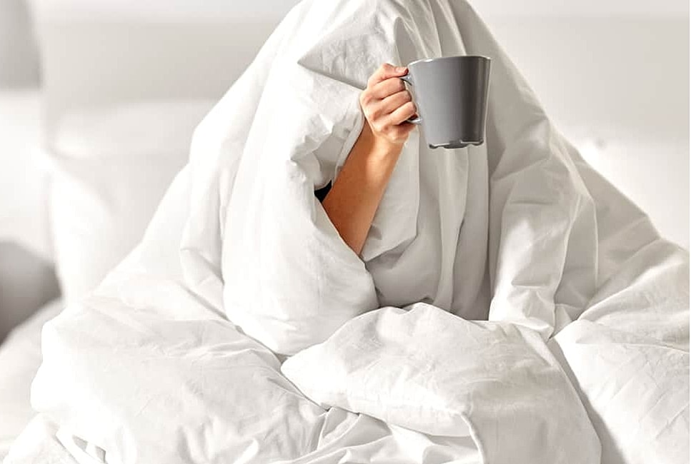 Person under blanket holding a coffee cup.
