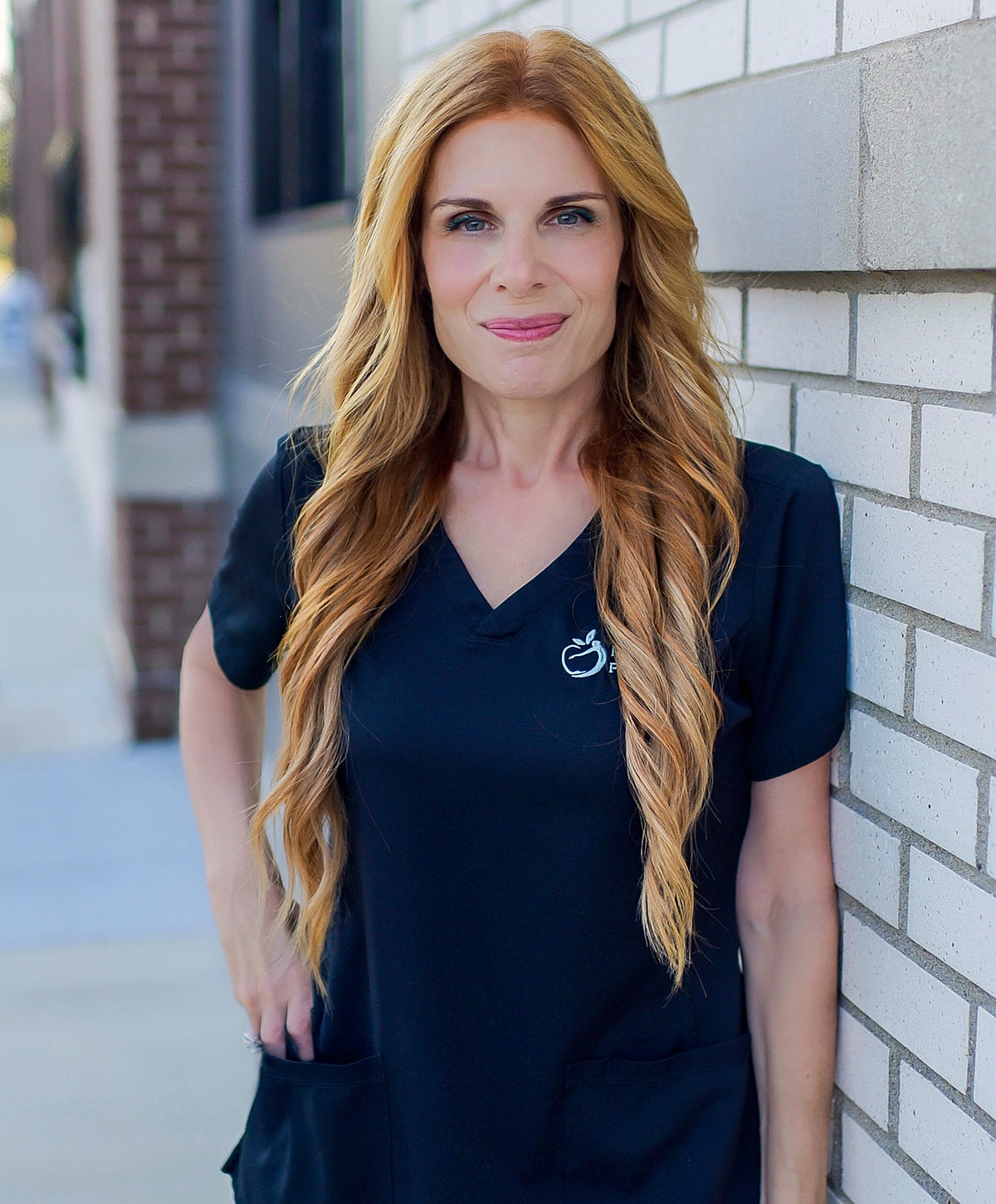 Woman in black scrubs standing by brick wall.