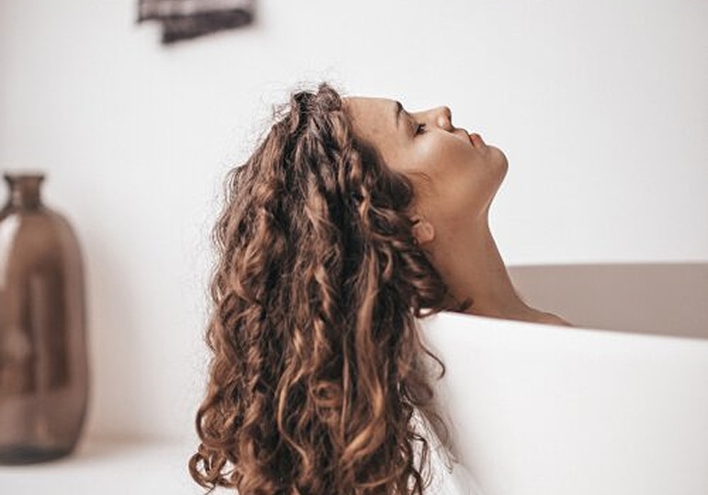 Woman relaxing in a bathtub with curly hair.