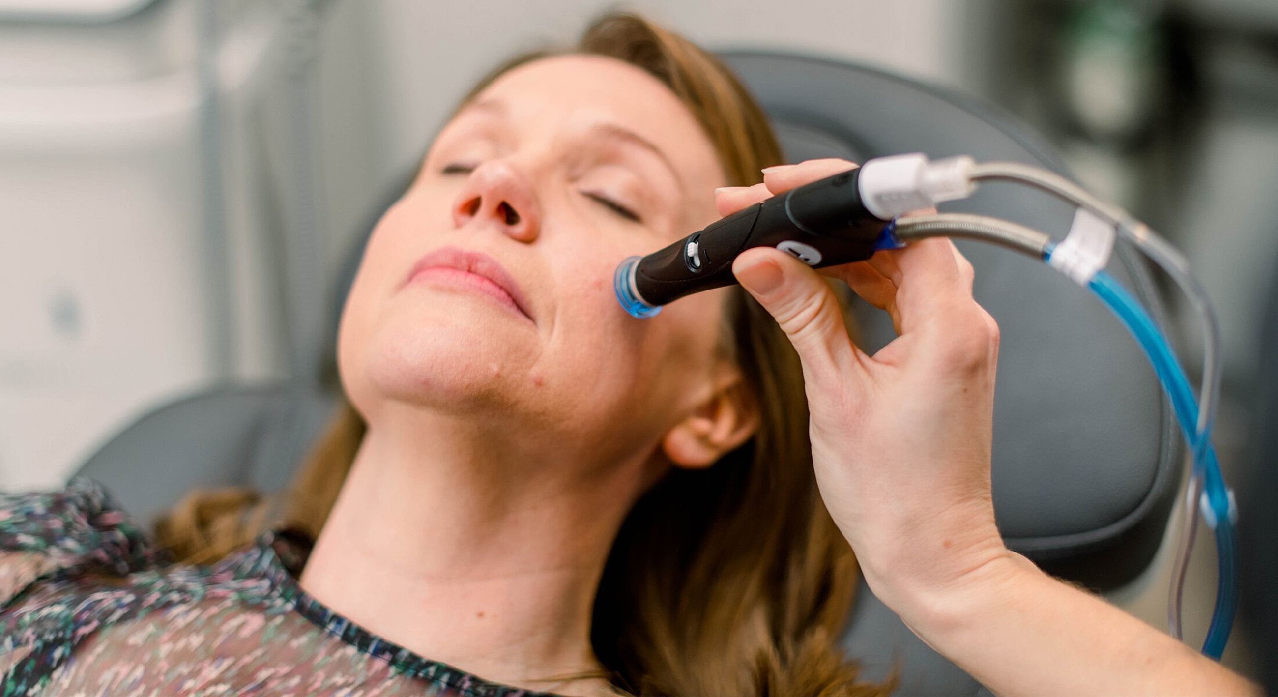 Woman receiving facial treatment with a device.