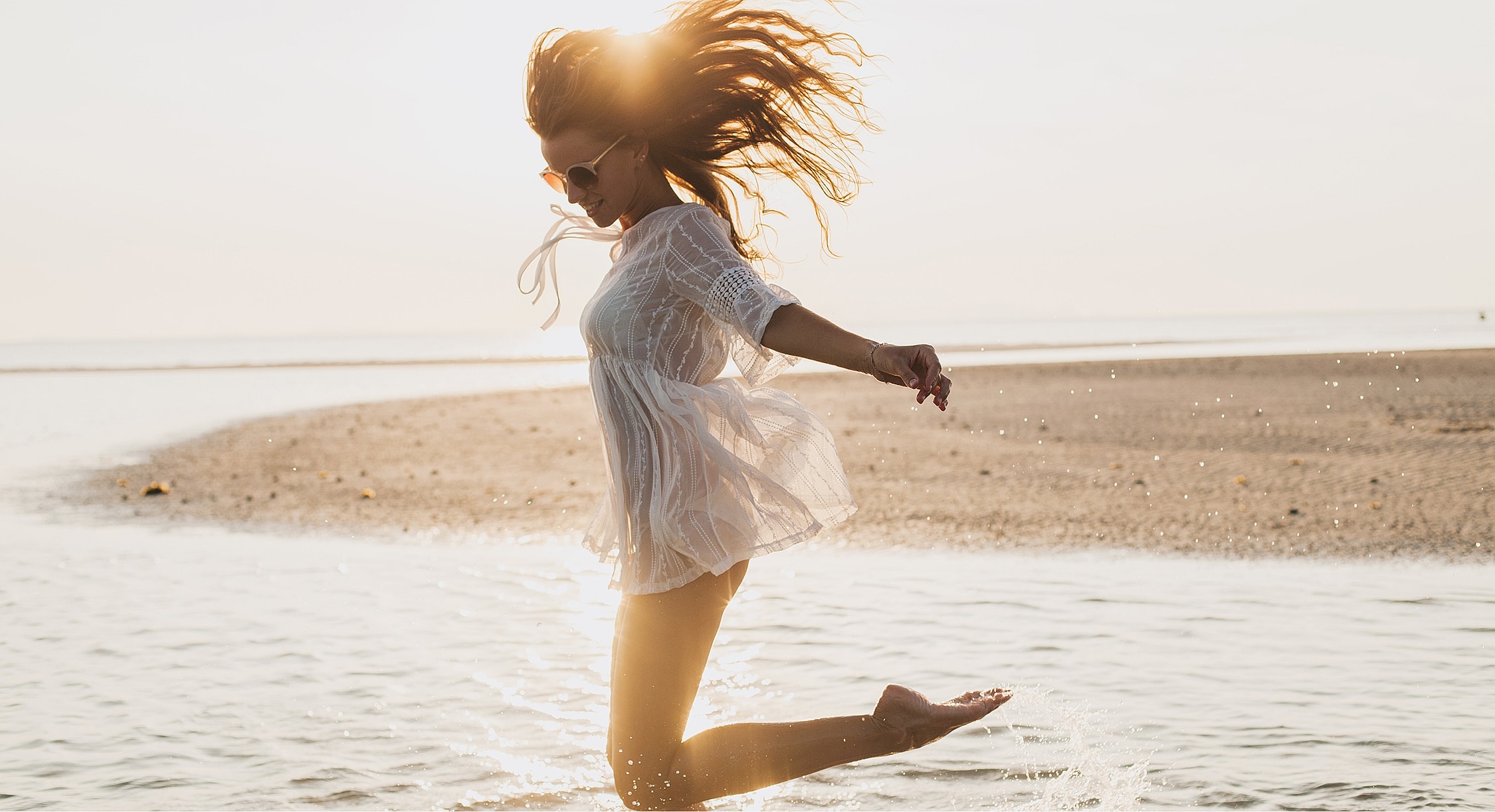 Woman joyfully jumping in shallow water.