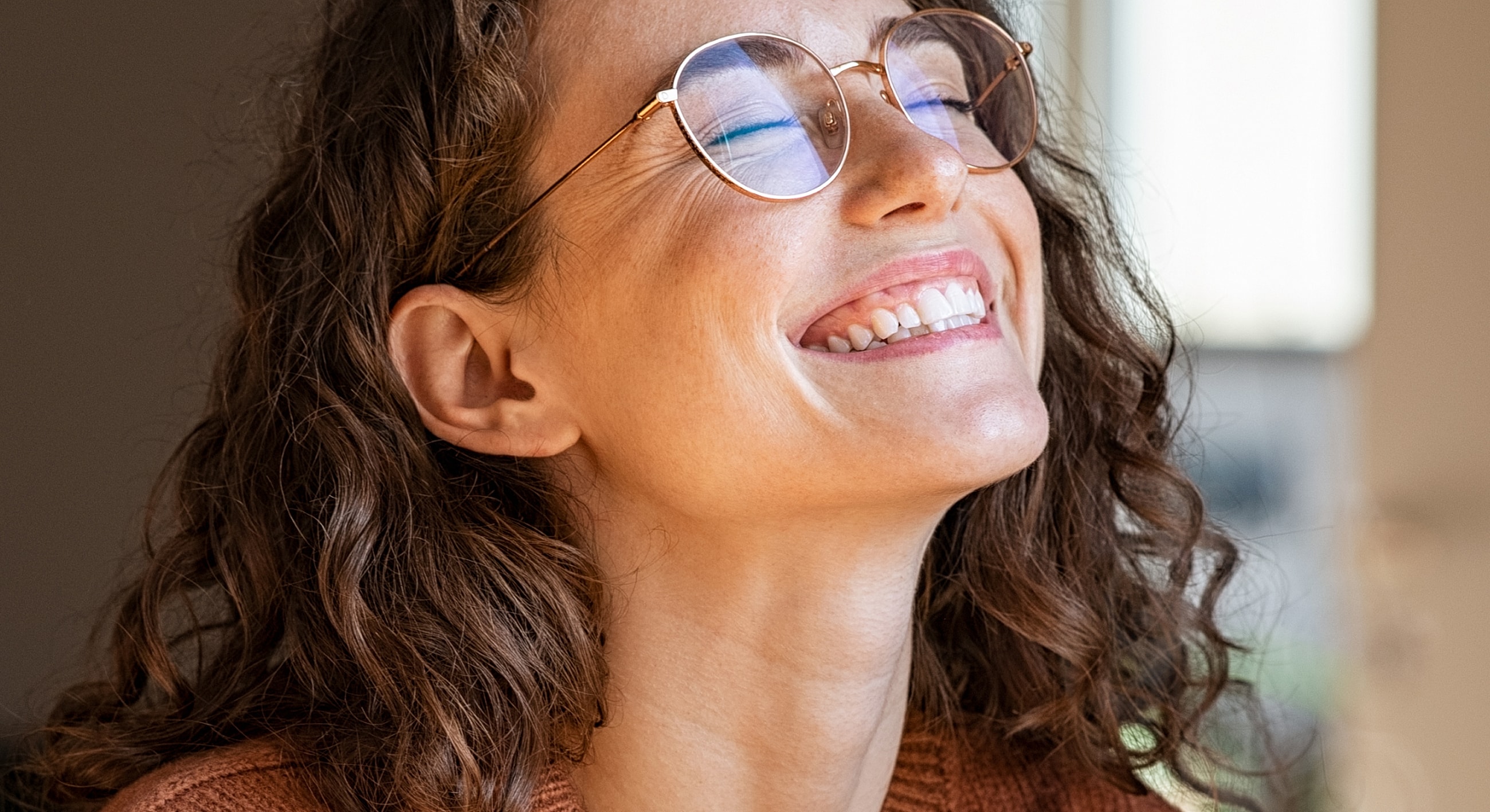 Smiling microneedling patient model with curly hair and glasses.