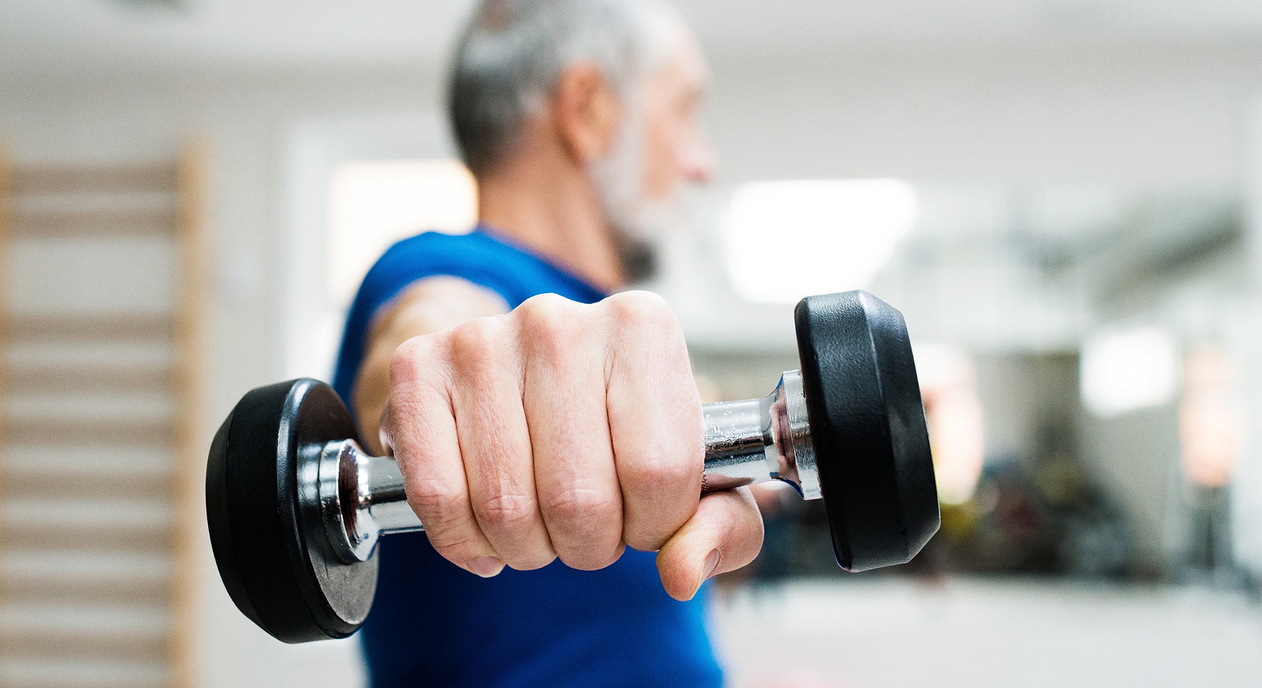 Elderly person lifting a dumbbell in gym.