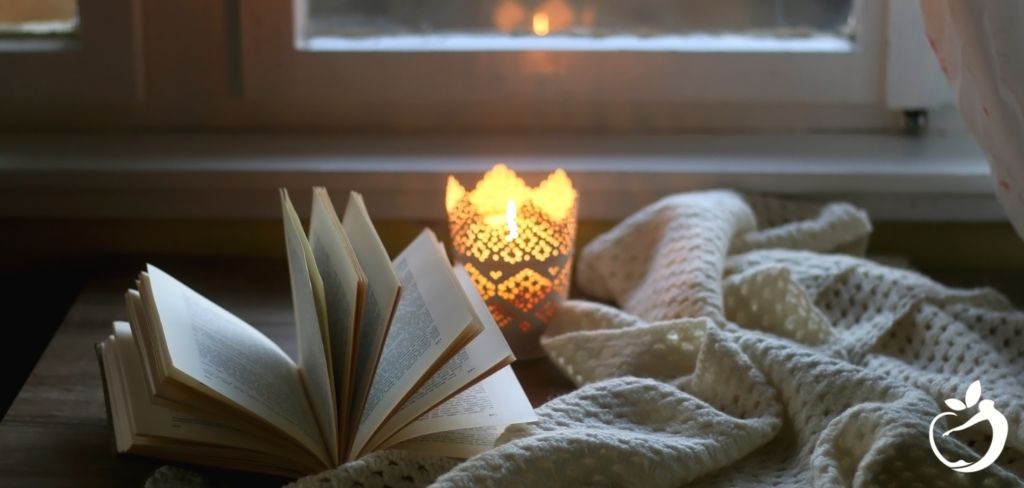 a book, candle, and blanket by a window