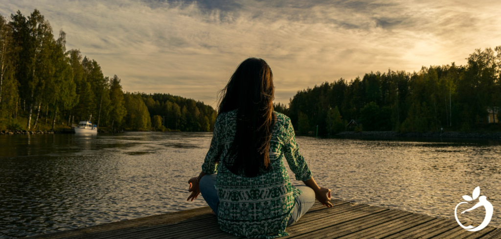 woman sitting on a dock at sunset meditating