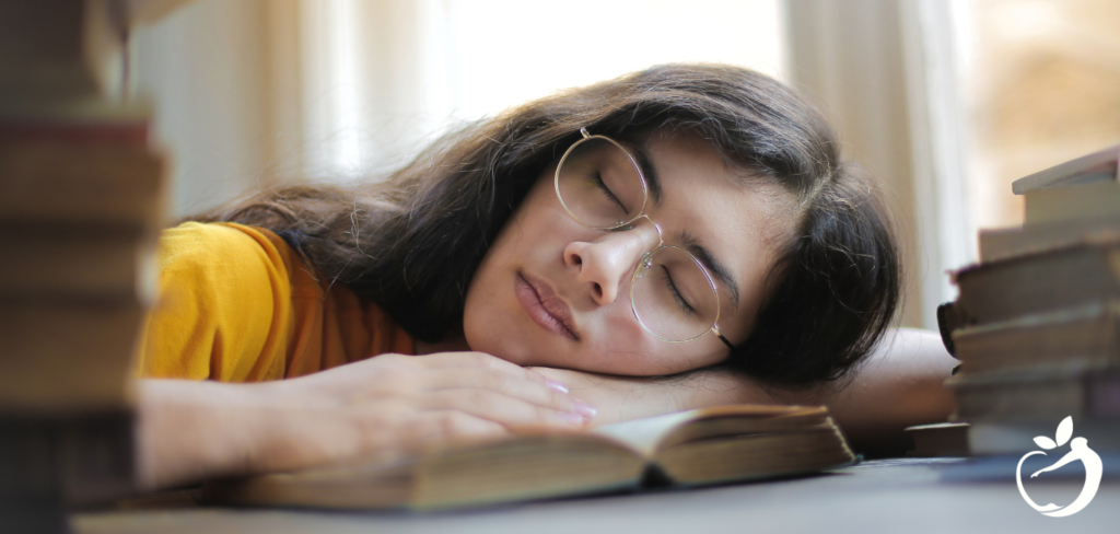 women wih her head down on a book at a desk while she's sleeping