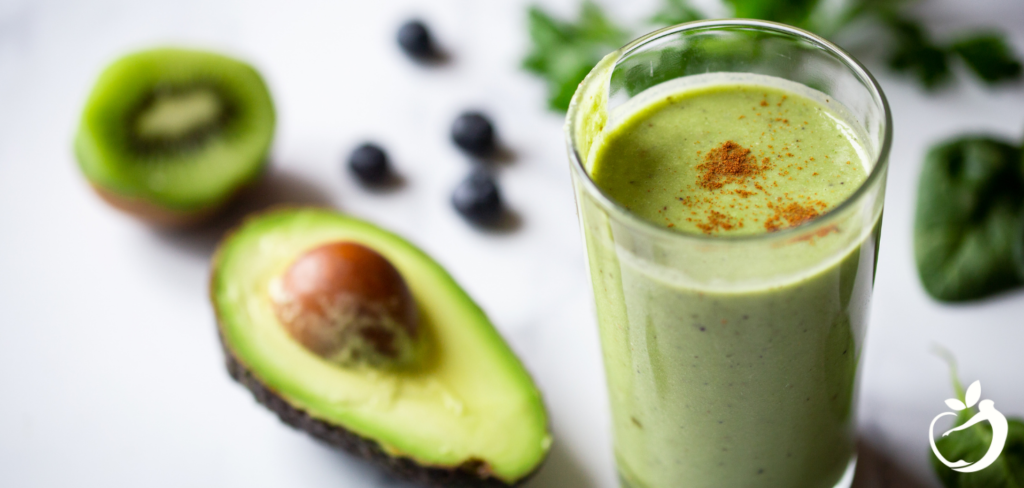 green smoothie with cinnamon sprinkled on top with avocado and kiwi next to it