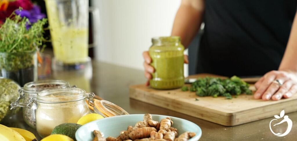 man holding a glass of green smoothie with smoothie ingredients around him