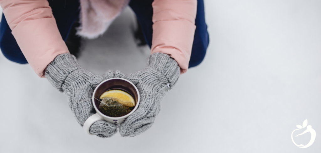 Showing an image of a person with mittens on holding a cup of tea. Staying healthy during the holidays.