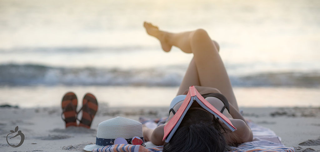 woman laying down at a beach with her legs crossed and a book over her face