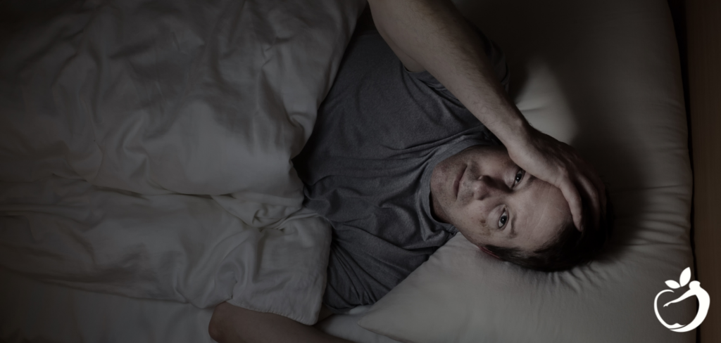 man in bed staring up at the ceiling, not able to sleep and holding his head