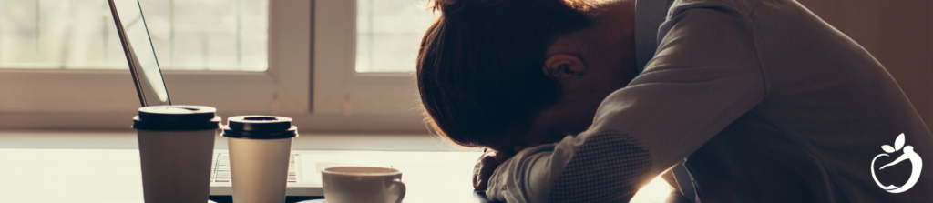 woman sitting in front of her laptop with cups of coffee resting her head down on her arm