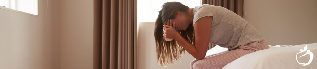 Woman sitting at the end of her bed with face in her hands