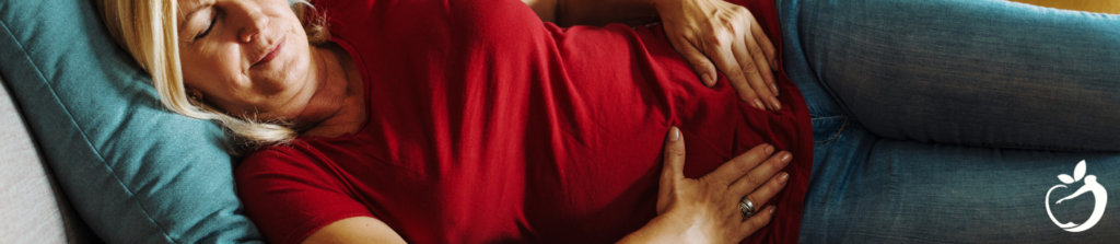 woman in a red shirt and jeans pressing down on her abdoman while laying on a couch