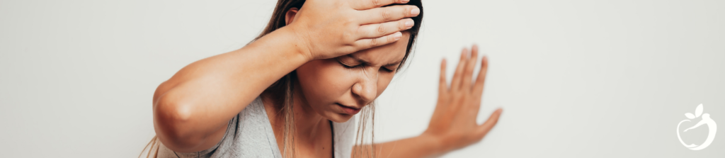 woman bracing herself against a wall with a hand on her forehead and her eyes closed