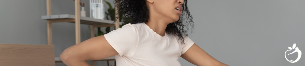 a woman wearing a white shirt grimacing and holding her hip