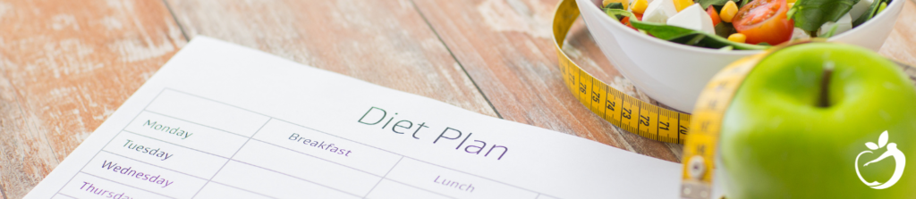 a diet plan log, apples, and salad on a table