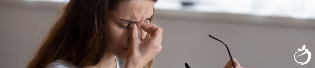 Image of a woman experiencing fatigue, pinch ing the bridge of her nose.