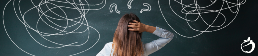 Image of a woman standing in front of a chalkboard with a bunch of scribbles and question marks on it.