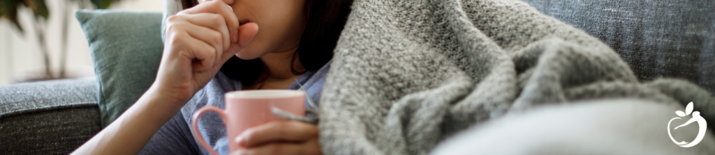 woman laying on a couch coughing and holding a cup of tea