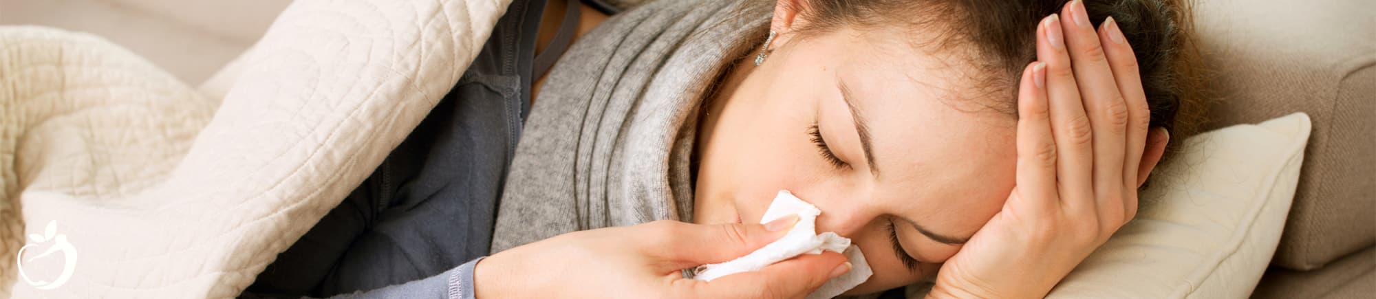 woman laying on a couch with her eyes closed blowing her nose