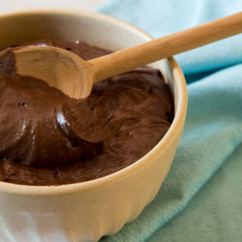 Recipe Post Header Image - Chocolate Avocado Pudding. Image of pudding in a bowl with a wooden spoon.