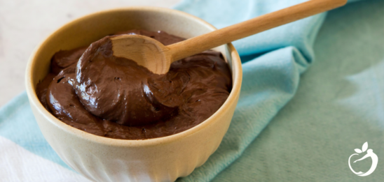 Recipe Post Header Image - Chocolate Avocado Pudding. Image of pudding in a bowl with a wooden spoon.